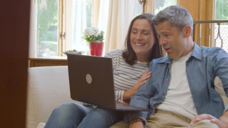 Sliding-Shot-of-Middle-Aged-Couple-Talking-and-Laughing-into-Laptop-During-Video-Call
