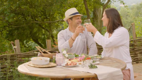 Wide-Shot-of-Middle-Aged-Couple-Bringing-Glasses-Together-During-Alfresco-Dinner