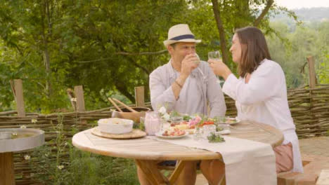Weitwinkelaufnahme-Eines-Paares-Mittleren-Alters,-Das-Seine-Gläser-Während-Des-Abendessens-Im-Freien-Zusammenbringt
