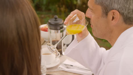 High-Angle-Shot-of-Middle-Aged-Man-Talking-to-Wife-During-Outdoor-Breakfast