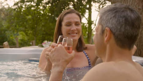 Over-the-Shoulder-Shot-of-Middle-Aged-Woman-Drinking-Champagne-In-Hot-Tub-with-Husband