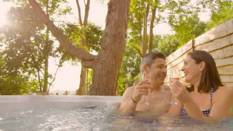 Wide-Shot-of-Middle-Aged-Couple-Drinking-Champagne-In-Hot-Tub-
