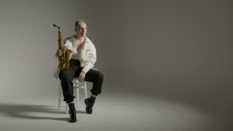 Wide-Angle-Shot-of-Model-Posing-with-Saxophone-Against-Grey-Backdrop
