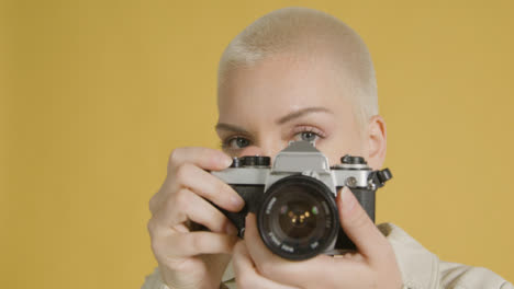 Woman-looks-into-lens-and-takes-photograph-on-vintage-camera