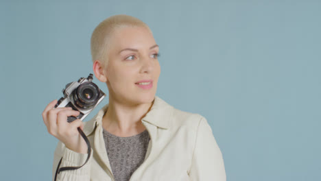 Weibliches-Kaukasisches-Model-Posiert-Mit-Vintage-Spiegelreflexkamera-Vor-Blauem-Hintergrund-03