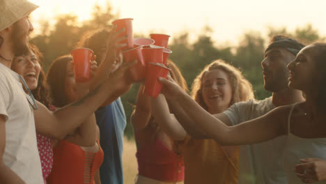 Mittlere-Aufnahme-Einer-Gruppe-Von-Freunden,-Die-Bei-Sonnenuntergang-Ihre-Plastikbierbecher-Anstoßen