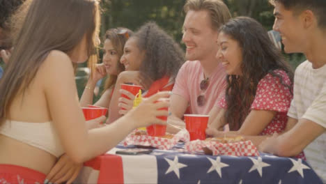 Sliding-Shot-of-Group-of-American-Friends-Sitting-Around-Table-Talking-and-Drinking
