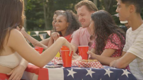 Sliding-Shot-of-a-Group-of-American-Friends-Sitting-Around-Table-Talking-and-Drinking