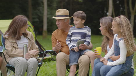 Toma-De-Seguimiento-De-La-Familia-En-Un-Viaje-De-Campamento-Sentado-Y-Hablando-Junto-A-Sus-Carpas-03