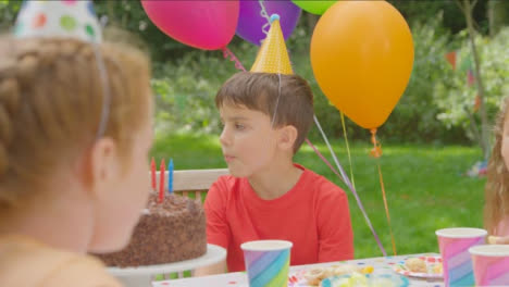 Pull-Focus-Shot-of-Children-Sitting-at-Table-at-Outdoor-Birthday-Party-