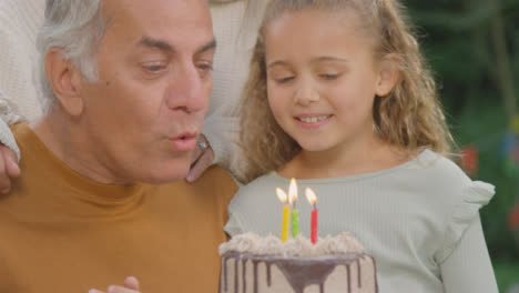 Handheld-Close-Up-Shot-of-Children-Helping-Their-Grandad-Blow-Out-Candles-On-Birthday-Cake