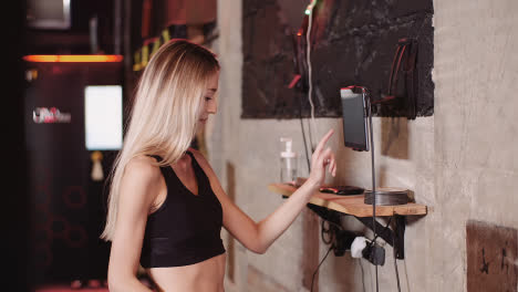 Slow-Motion-Of-Female-Athlete-Choosing-Music-On-Digital-Tablet-Mounted-At-Wall-In-Fitness-Club