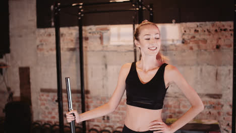Slow-Motion-Of-Smiling-Sporty-Young-Woman-Holding-Barbell-While-Standing-With-Hand-On-Hip-At-Gym