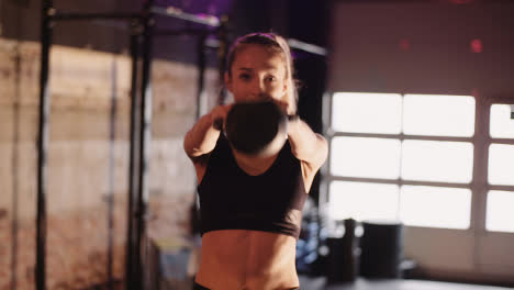 Confident-Young-Woman-Exercising-With-Kettlebell-During-Training-At-Gym