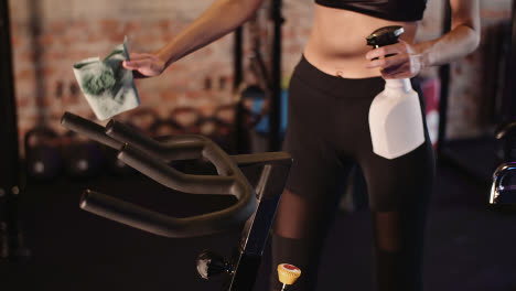 Midsection-Of-Female-Trainer-Cleaning-Handle-Of-Cycling-Bike-At-Health-Club