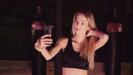 Female-Athlete-Adjusting-Hair-While-Taking-Selfie-Through-Smartphone-At-Fitness-Studio
