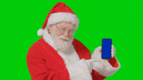Porträtaufnahme-Des-Weihnachtsmanns,-Der-Ein-Bluescreen-Handy-Vor-Dem-Greenscreen-Hält