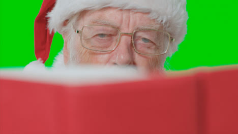 Close-Up-Shot-of-Santa-Reading-Red-Book-In-Front-of-a-Green-Screen