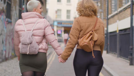Tracking-Shot-Following-Two-Young-Women-Holding-Hands-and-Walking-Down-an-English-Street