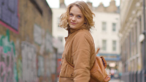 Tracking-Shot-Following-Young-Woman-Walking-Down-an-Urban-Street-and-Smiling-Back-to-Camera