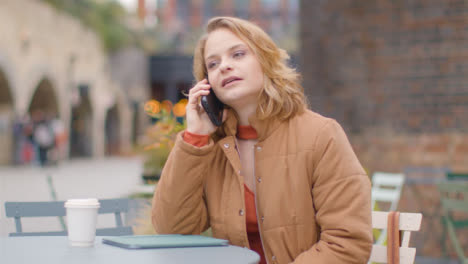 Medium-Shot-of-Young-Woman-Sitting-at-Outdoor-Table-Talking-On-Phone