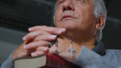 Low-Angle-Shot-of-Senior-Man-Praying-with-Rosary-Beads-and-Bible