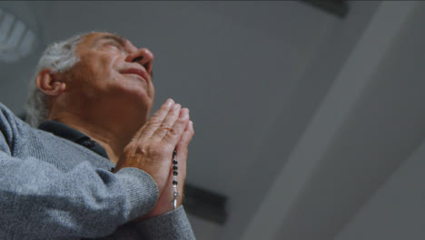 Low-Angle-Shot-of-Senior-Man-Praying-with-Rosary-Beads