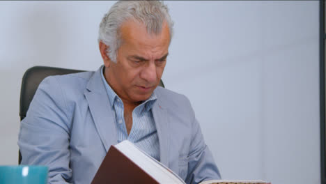 Flachwinkelaufnahme-Eines-älteren-Mannes,-Der-Ein-Buch-An-Einem-Schreibtisch-Liest