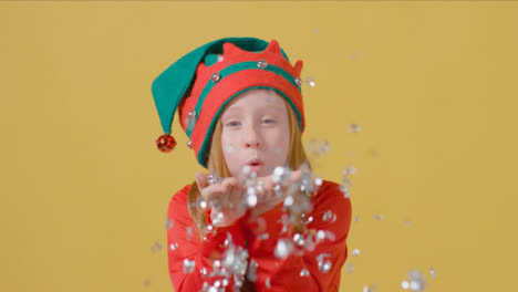 Young-Girl-in-Elf-Hat-Blows-Tinsel-at-Camera