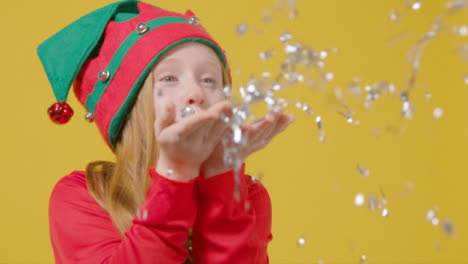 Close-Up-of-Festive-Girl-in-Elf-Hat-Blows-Tinsel