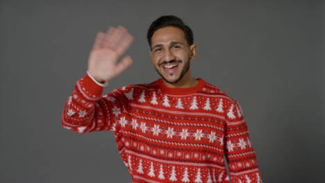 Portrait-Shot-of-Young-Man-In-Christmas-Sweater-Waving-and-Smiling