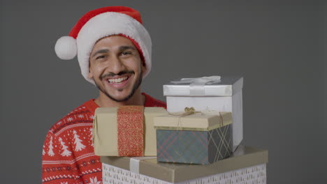 Portrait-Shot-of-Young-Man-Holding-Pile-of-Gifts-Saying-Merry-Christmas