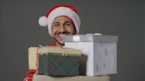 Portrait-Shot-of-Young-Man-Holding-Pile-of-Gifts-to-the-Camera-and-Saying-Merry-Christmas