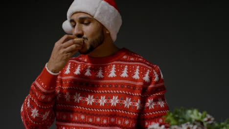 Low-Angle-Shot-of-Young-Man-In-Christmas-Sweater-Eating-a-Mince-Pie