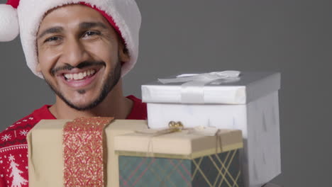 Close-Up-Shot-of-Young-Man-Holding-Pile-of-Christmas-Gifts-Saying-Merry-Christmas