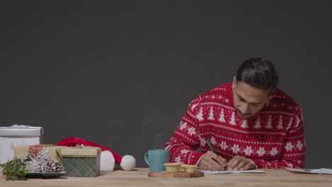 Wide-Shot-of-Young-Man-In-Christmas-Sweater-Writing-Christmas-Cards