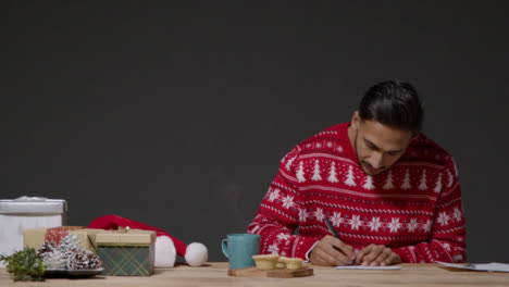 Wide-Shot-of-a-Young-Man-In-Christmas-Sweater-Writing-Christmas-Cards
