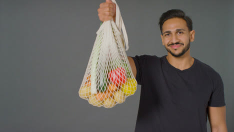 Portrait-Shot-of-Young-Man-Holding-Up-Bag-of-Vegetables-with-Copy-Space
