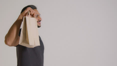 Mid-Side-Shot-of-Man-Holding-Up-Paper-Bag-and-Smiling-