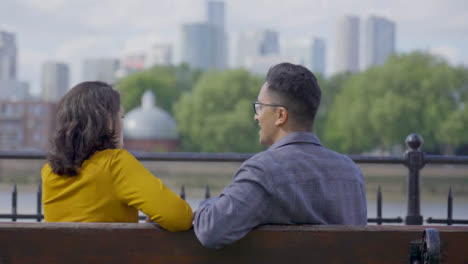 Mid-Shot-of-Couple-Sitting-on-Bench-Talking-Against-City-Skyline