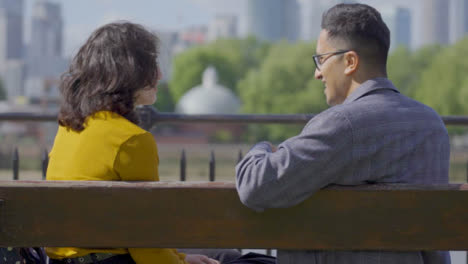 Mid-Shot-of-Couple-Sit-and-Talk-on-Bench-Against-City-Skyline