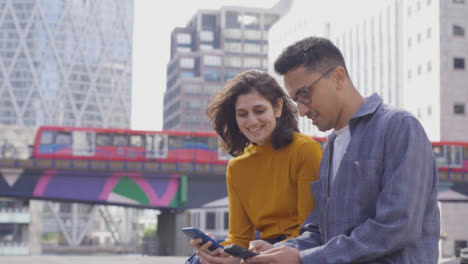 Mittenaufnahme-Von-Zwei-Studenten,-Die-Sich-Unterhalten-Und-Telefone-Mit-Stadtkulisse-Benutzen