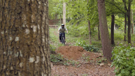 Toma-En-Cámara-Lenta-Del-Hombre-En-Bicicleta-De-Montaña-Haciendo-Saltos-En-El-Aire-En-Un-Camino-De-Tierra-A-Través-Del-Bosque