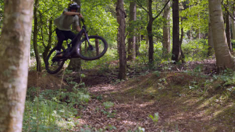 Slow-Motion-Shot-Of-Man-On-Mountain-Bike-Making-Mid-Air-Jumps-On-Dirt-Trail-Through-Woodland