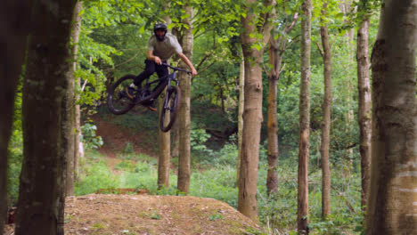 Hombre-Disparado-En-Cámara-Lenta-En-Bicicleta-De-Montaña-Haciendo-Salto-En-El-Aire-En-Un-Sendero-De-Tierra-A-Través-Del-Bosque