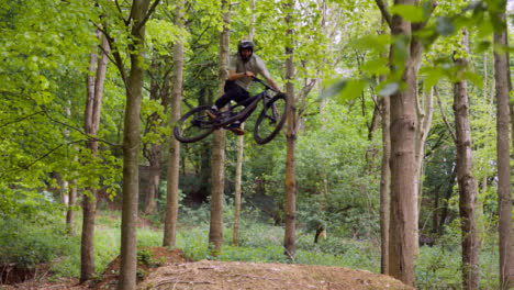 Slow-Motion-Shot-Man-On-Mountain-Bike-Making-Mid-Air-Jump-On-Dirt-Trail-Through-Woodland-2