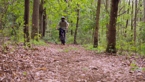 Toma-En-Cámara-Lenta-Del-Hombre-En-Bicicleta-De-Montaña-Y-Haciendo-Caballito-A-Lo-Largo-Del-Sendero-A-Través-Del-Bosque