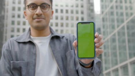 Low-Angle-Shot-of-a-Young-Man-Holding-Green-Screen-Smartphone