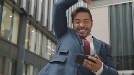 Excited-Businessman-Outside-Office-Holding-Mobile-Phone-Celebrating
