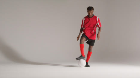 Studio-Portrait-Of-Young-Male-Footballer-Wearing-Club-Kit-Dribbling-With-Ball-